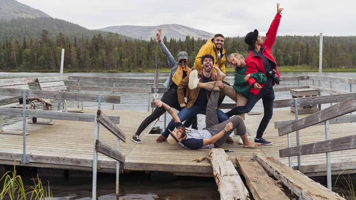 Finland, Lapland, Portrait Of Happy Playful Friends Posing On Jetty At A Lake